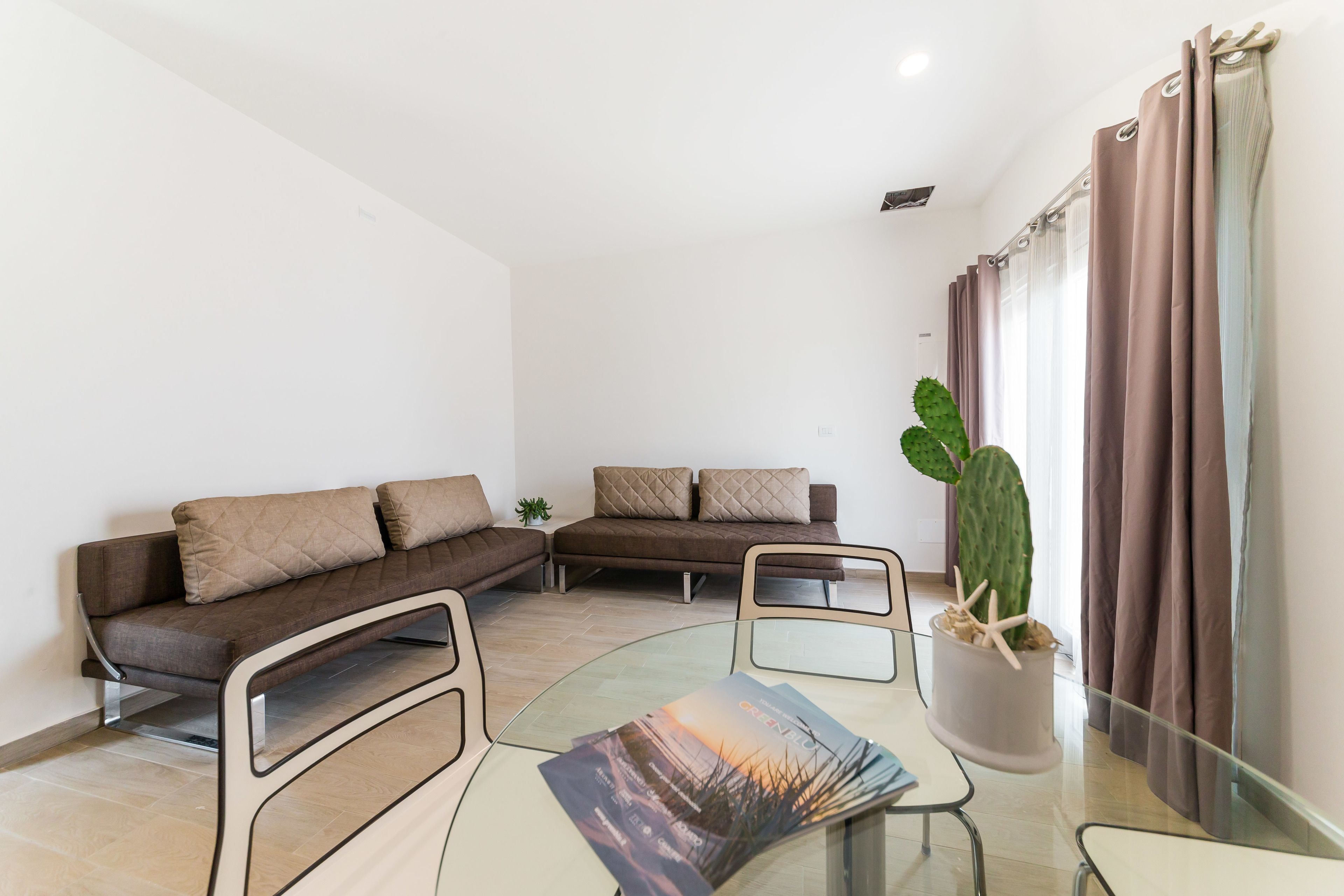 Een moderne woonkamer met twee banken, een glazen salontafel en een potplant.