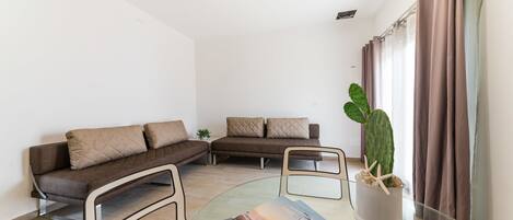 Een moderne woonkamer met twee banken, een glazen salontafel en een potplant.