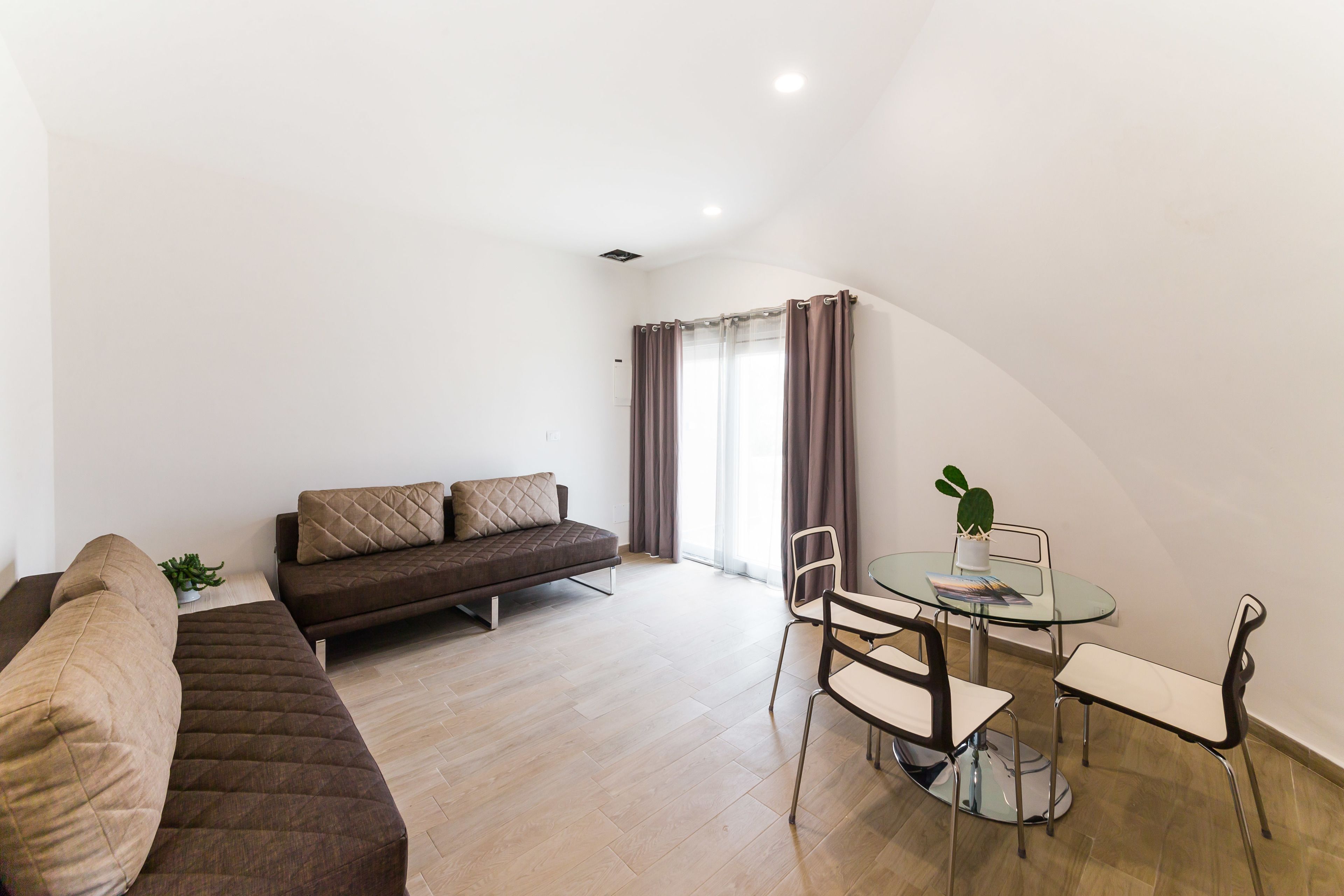 Una sala de estar moderna con un sofá, una mesa de comedor con sillas y una planta en maceta.