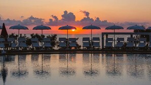A poolside area with lounge chairs and umbrellas during sunset.