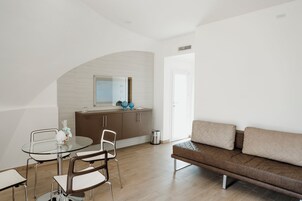 Un soggiorno moderno con un tavolo da pranzo in vetro, un divano marrone e una zona cucina con piano di lavoro e pensili bianchi.