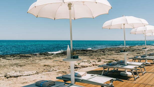 A beachside area with white umbrellas and lounge chairs, a wooden deck, and a view of the ocean.