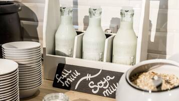 A breakfast bar with stacks of white plates, a sign indicating full milk and soy milk options, and bottles of Absolut Pure Milk.