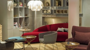 A modern living room with a red sofa, grey armchairs, and a red pendant light. There are shelves with decorative items and a sign that reads "BIRGSPLAZT". - Holiday Inn - the niu, Franz Vienna by IHG (Vienna)