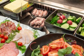 Un buffet proposant une variété de plats, notamment des viandes et fromages en tranches, ainsi que des légumes frais.