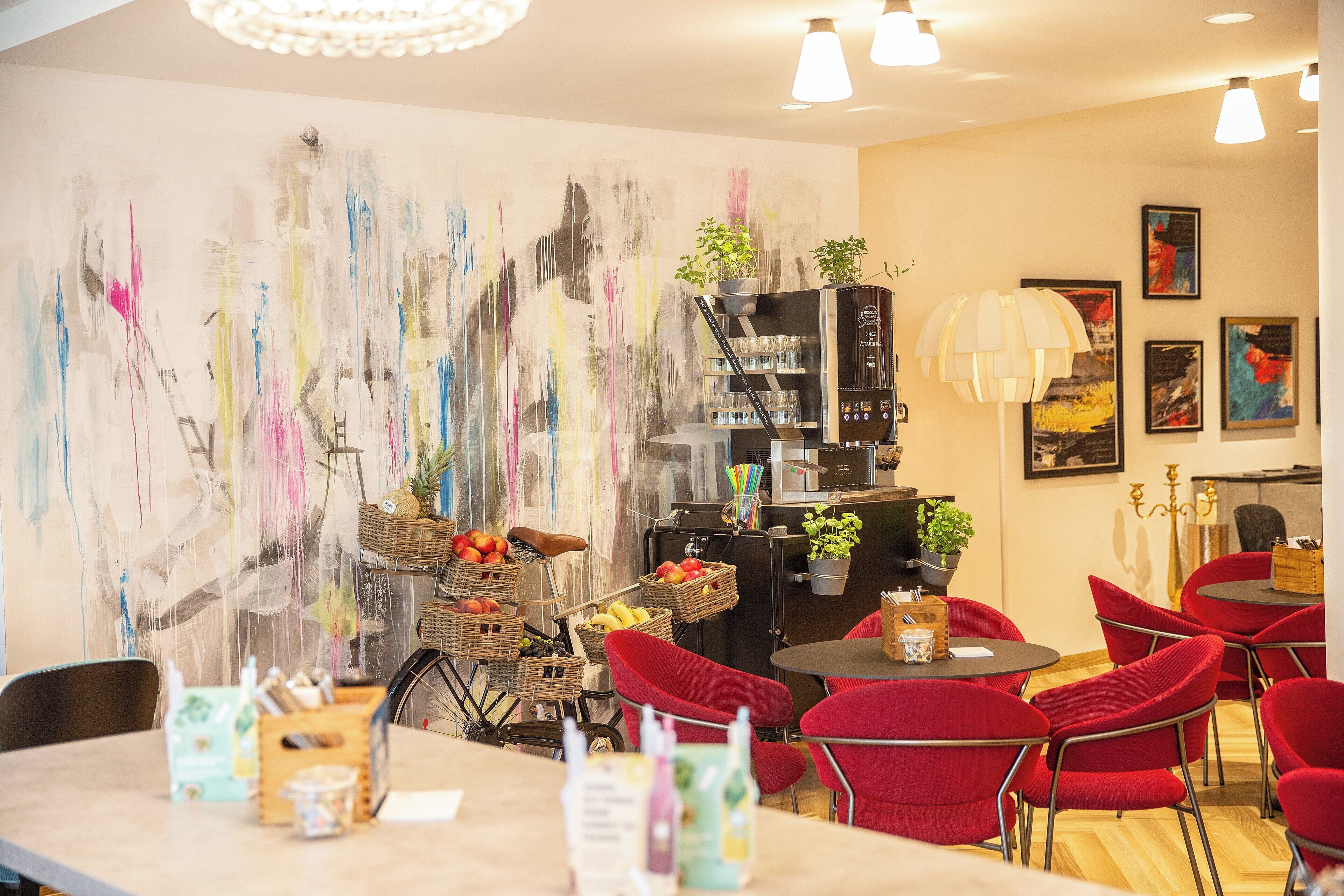 A modern cafe with red chairs, a coffee machine, and a wall with abstract art.