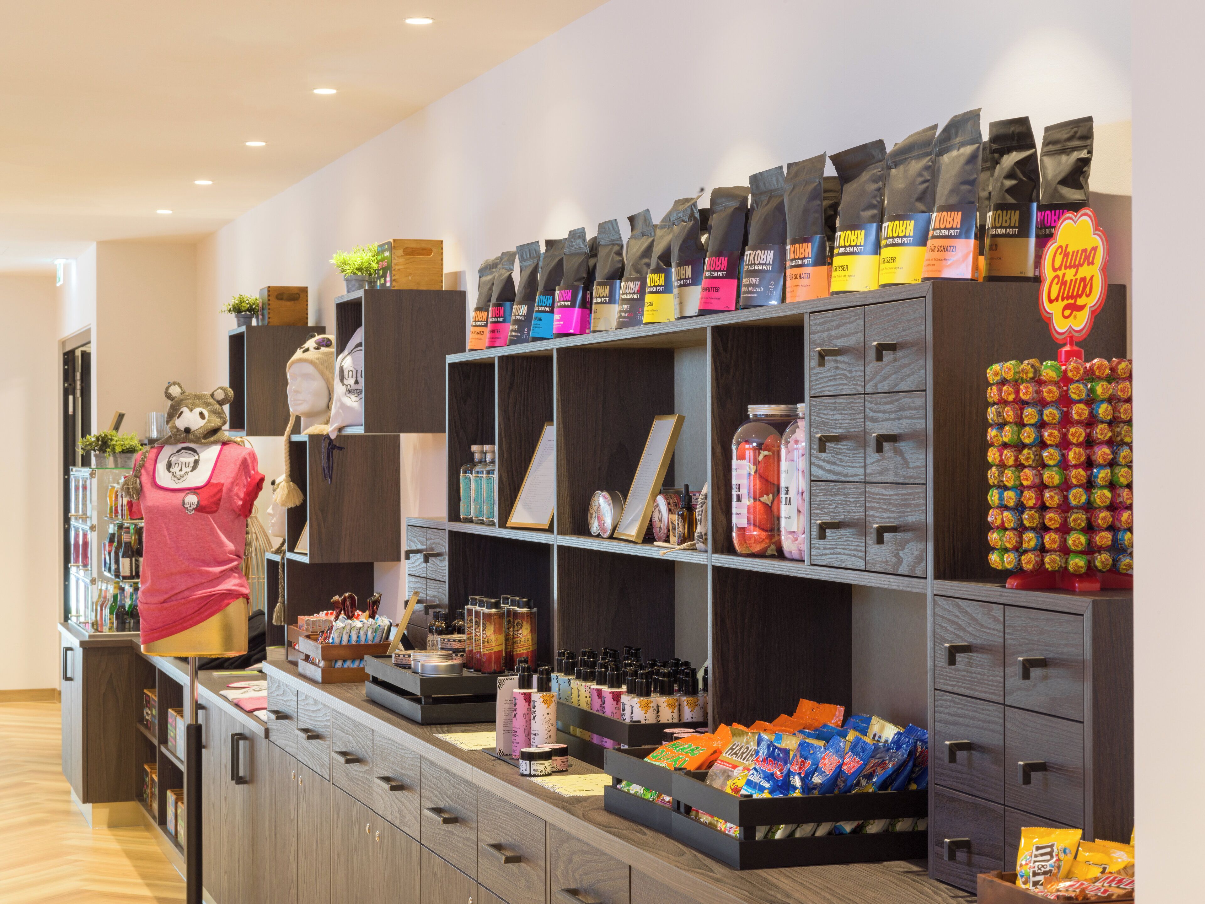 A retail store with shelves stocked with various products, a display of packaged goods, and a mannequin dressed in a bear costume.