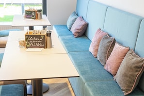 A modern living area with a sofa, cushions, a table with a chalkboard sign, and a window with a view. - Holiday Inn - the niu, Franz Vienna by IHG (Vienna)