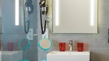 Un baño con un lavabo blanco, dos vasos rojos, un espejo turquesa y un secador de pelo montado en la pared.