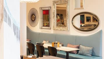 A dining area with a blue cushioned bench, a table, and chairs. There are decorative mirrors and wall art on the wall.