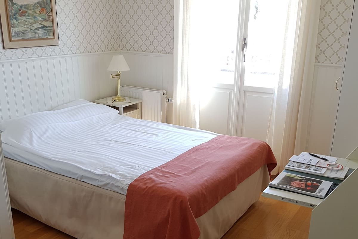 A neatly arranged bedroom with a bed, bedside table, lamp, and a window with curtains.