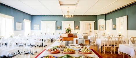 A banquet hall with multiple tables set for a meal, a buffet with various dishes, and a chandelier.