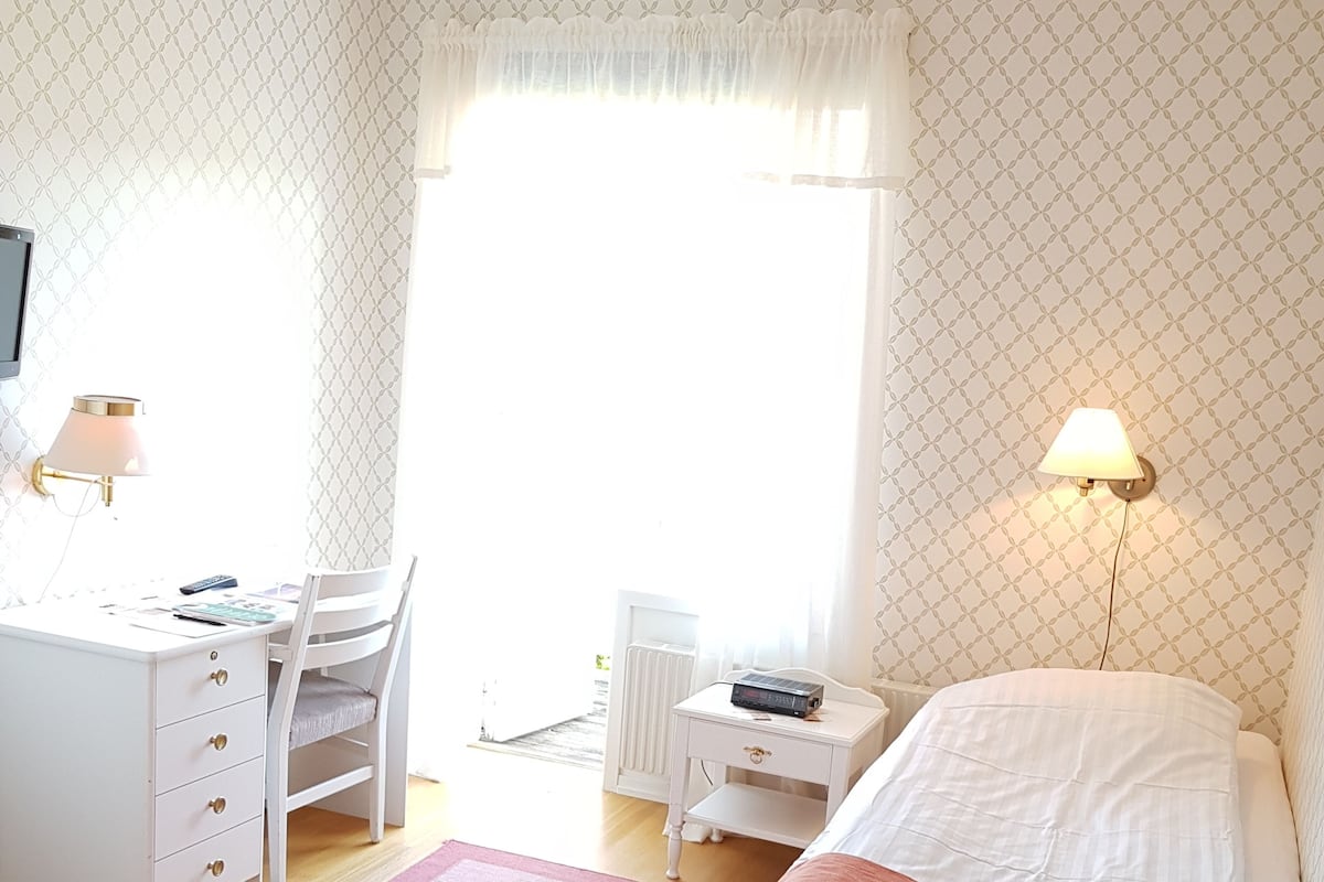 A bedroom with a bed, a desk, a chair, a nightstand, and a lamp.