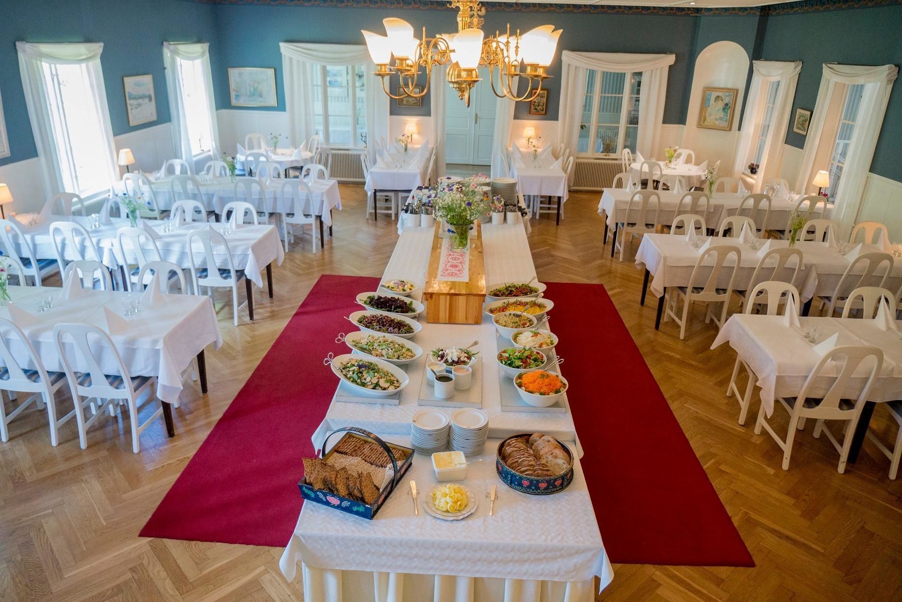 A banquet hall with multiple round tables covered with white tablecloths, arranged in rows.