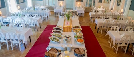 A banquet hall with multiple round tables covered with white tablecloths, arranged in rows.