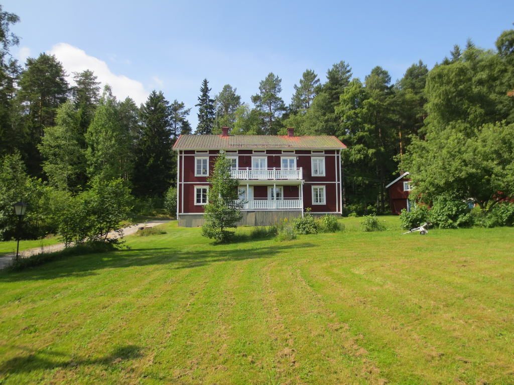 A large, two-story building with a red facade and white trim, surrounded by a well-maintained lawn and dense trees.