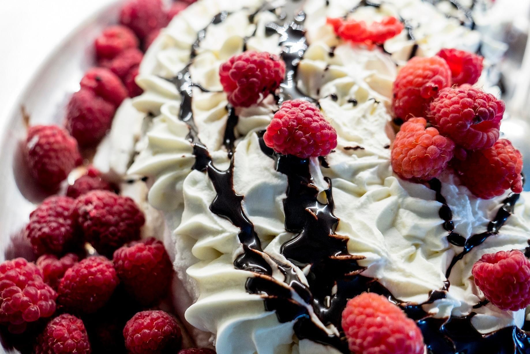 A dessert with whipped cream, chocolate drizzle, and raspberries.