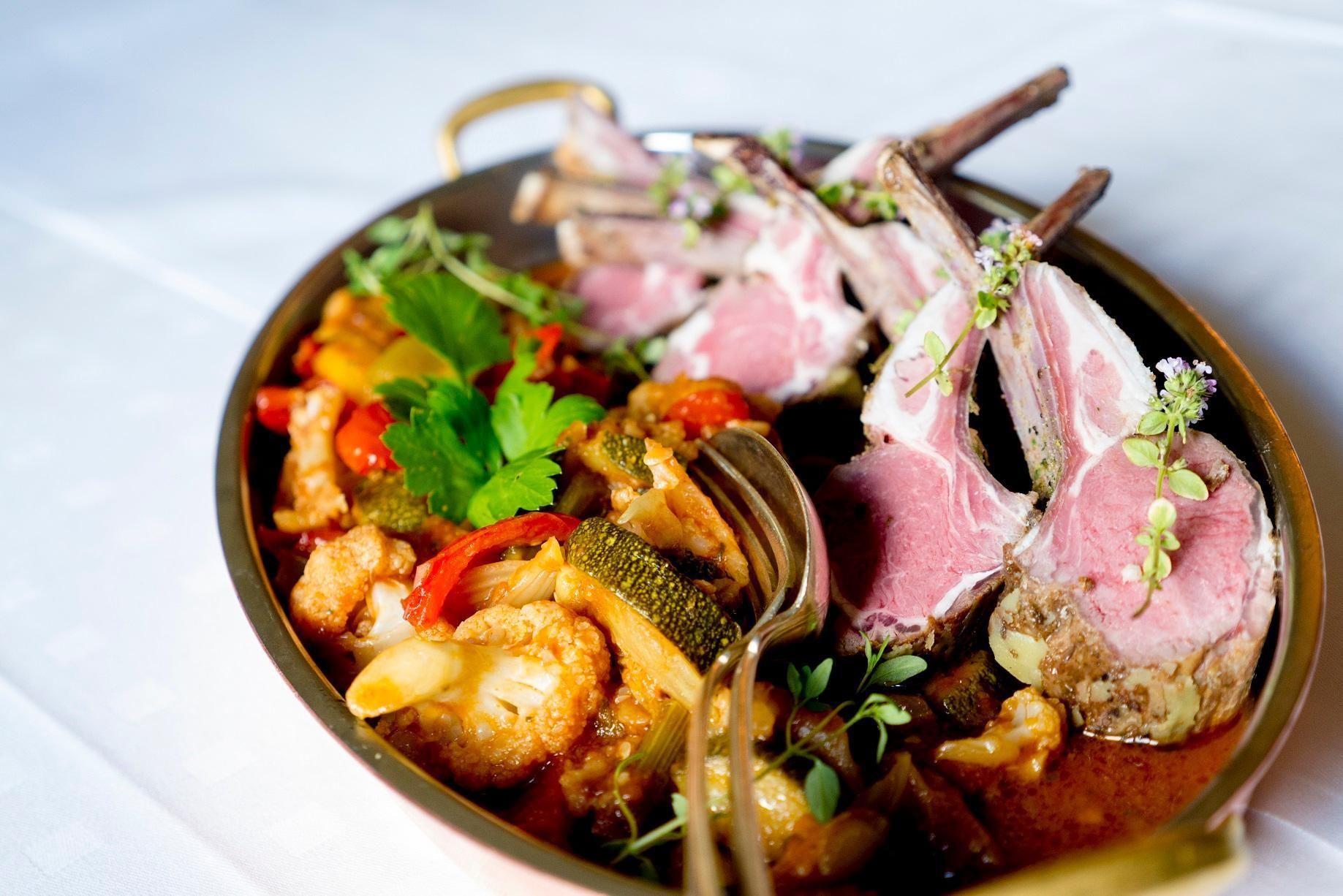 Un piatto con costolette d'agnello, verdure e erbe aromatiche.
