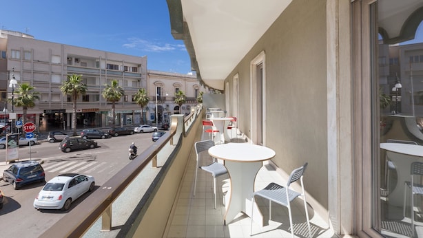 Ein Balkon mit Sitzgelegenheit im Freien, Blick auf eine Straße und eine Gebäudefassade.