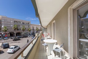 Un balcón con mobiliario exterior, vista a la calle y fachada de un edificio.