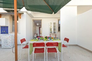 A dining area with a table set for four, surrounded by red chairs, under a green canopy. - Appartamento Corso Roma (Gallipoli)