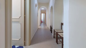A long, narrow hallway with a tiled floor, wooden chairs, and a door at the end. - Appartamento Turrita (Presicce-Acquarica)