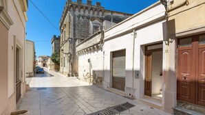 A narrow street with cobblestone pavement, a metal grate, and a building with a closed shutter and a wooden door. - Appartamento Turrita (Presicce-Acquarica)