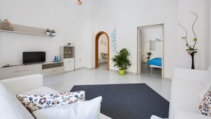 A modern living room with a flat-screen TV, white sofas, a coffee table, and a potted plant. - Casa Angiulina (San Pancrazio Salentino)