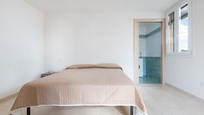 A bedroom with a bed, a door leading to a bathroom, and a window. - Casa di Pietro (Nardò)