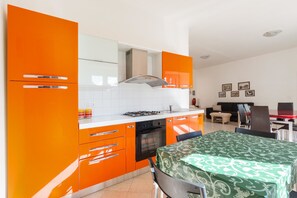 Eine Küche mit orangefarbenen Schränken, einem Gasherd und einem Essbereich mit einem grünen Tischlein.