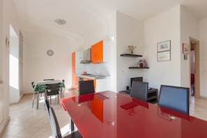 Eine moderne Küche mit weißen Schränken und orangefarbenen Akzenten, ein Essbereich mit einem roten Tisch und Stühlen sowie eine kleine Kücheninsel.