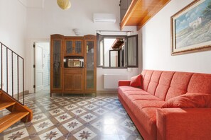 Una sala de estar con un sofá rojo, un aparador de madera, suelo de baldosas y un cuadro en la pared.