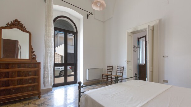 A bedroom with a bed, dresser, chairs, and a door leading outside. - Casa Graziella (Neviano)