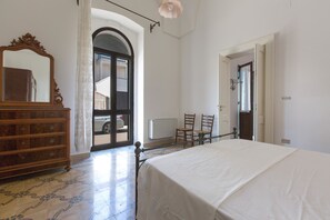 A bedroom with a bed, dresser, chairs, and a door leading outside.