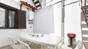 A white table with chairs, a window with brown shutters, and a red object on a stand. - Casa Graziella (Neviano)