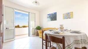 A dining area with a table set for two, a yellow chair, a potted plant, and a view of the outdoors. - Casetta del Glicine (Melendugno)