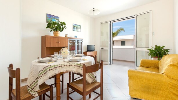 A dining area with a table set for four, a yellow sofa, and a sliding glass door leading to a balcony. - Casetta del Glicine (Melendugno)