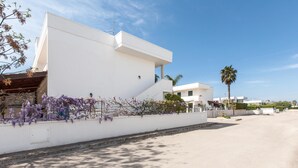 A modern building with a white exterior, a staircase leading to a flat roof, and purple flowering vines along the wall. - Casetta del Glicine (Melendugno)