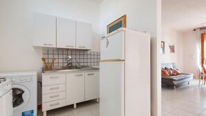 Une cuisine compacte avec des meubles blancs, un lave-linge encastré et un réfrigérateur.