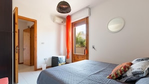 Une chambre à coucher avec un lit, une fenêtre avec des rideaux, une porte et un miroir fixé au mur.