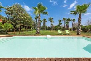 A swimming pool with a wooden deck, surrounded by palm trees and green lawn chairs. - Dependance di Villa Dea (Matino)