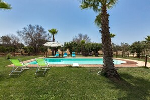 Un patio trasero con piscina, sillas de jardín verdes y una palmera.