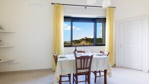 Comedor con mesa dispuesta para cuatro personas, sillas, ventana con cortinas y vistas al exterior.