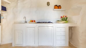 A kitchen with white cabinets, a sink, and a shelf with decorative items. - Il Giardino delle Cipolliane (Gagliano del Capo)