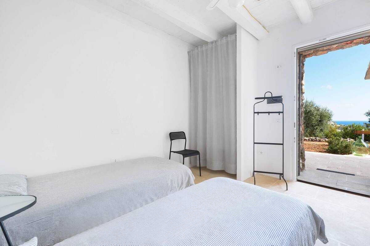 Ein Schlafzimmer mit zwei Betten, einem Sessel, einem Kleiderständer und Blick ins Freie.