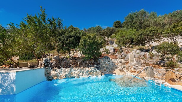 A clear blue pool surrounded by rocky terrain and trees. - Il Giardino delle Cipolliane (Gagliano del Capo)