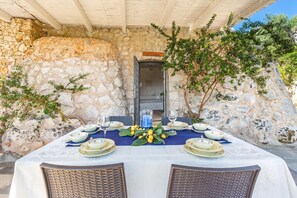 A table set for dining with plates, glasses, and a centerpiece, set against a stone wall with a door in the background. - Il Giardino delle Cipolliane (Gagliano del Capo)