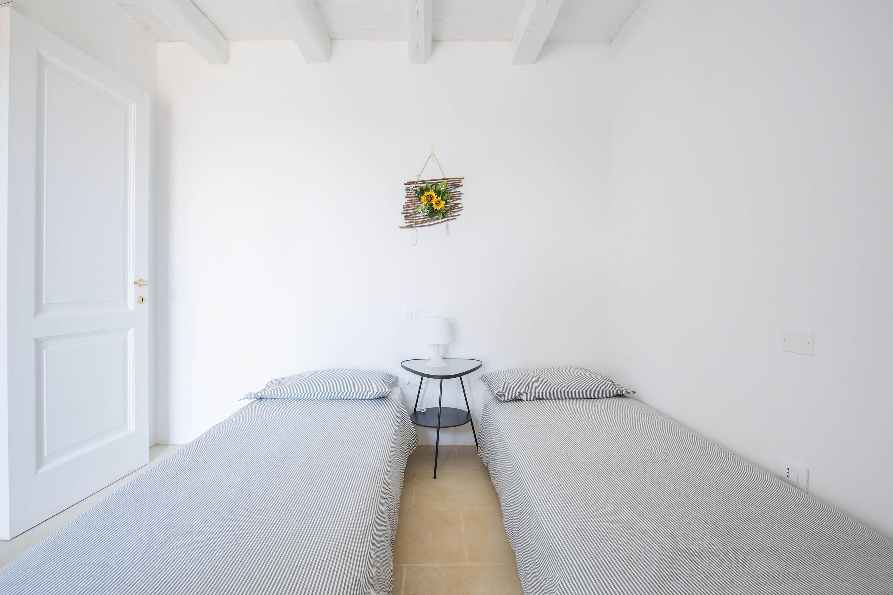 A small, clean room with two single beds, a small table, and a wall-mounted decoration.