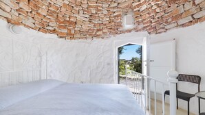 A bedroom with a brick ceiling, a white bed, a white door, and a balcony with a chair. - Il Giardino delle Cipolliane (Gagliano del Capo)
