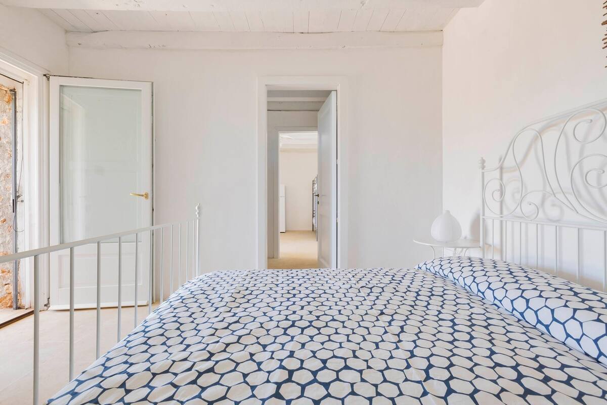 Ein Schlafzimmer mit einem gemusterten Bettbezug, einem weißen Metall-Kopfteil und einer weißen Tür.